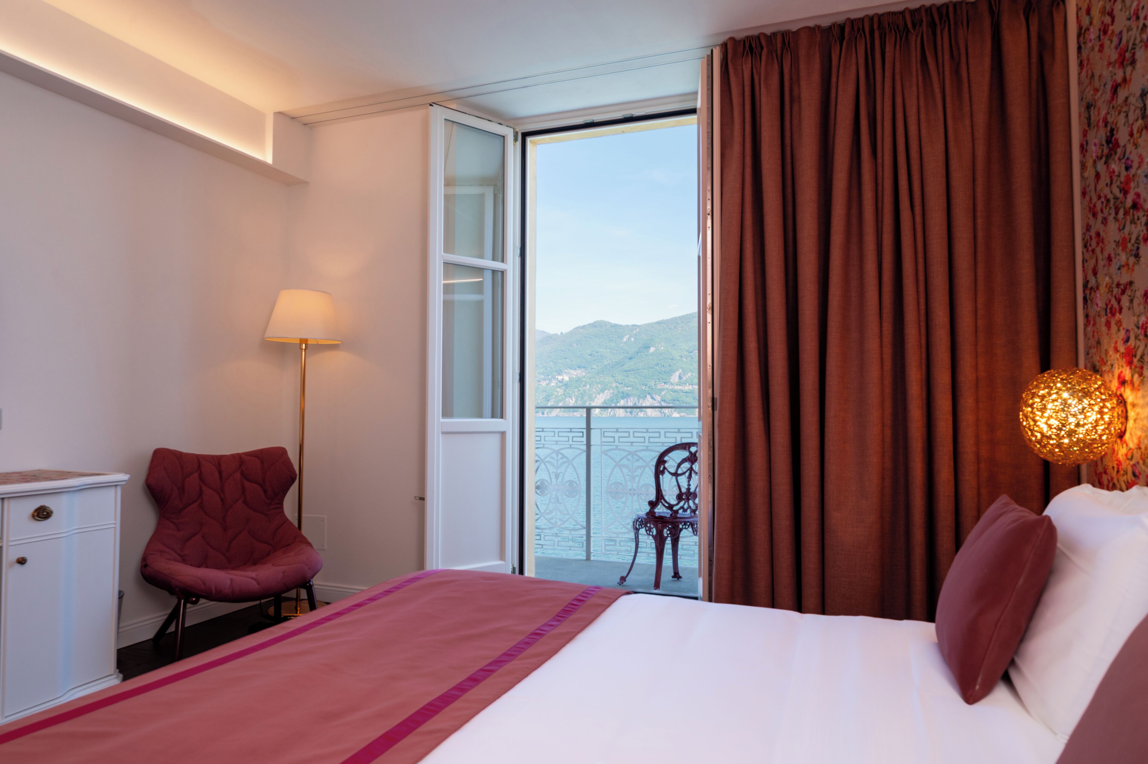 Une chambre d’hôtel avec un lit, une chaise, un bureau, une lampe et une vue sur la mer.