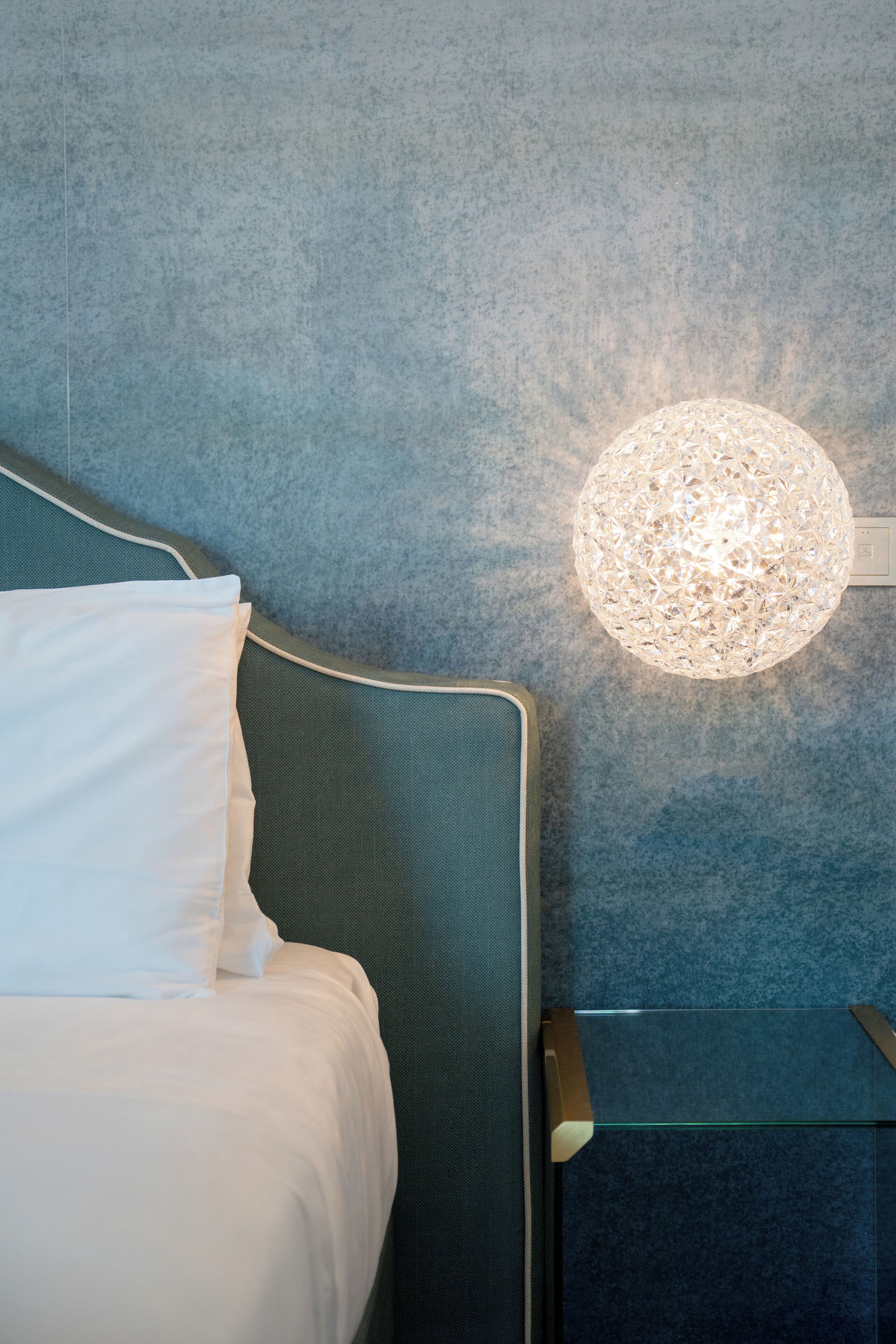 A bed with white bedding, a teal headboard, and a textured wall.