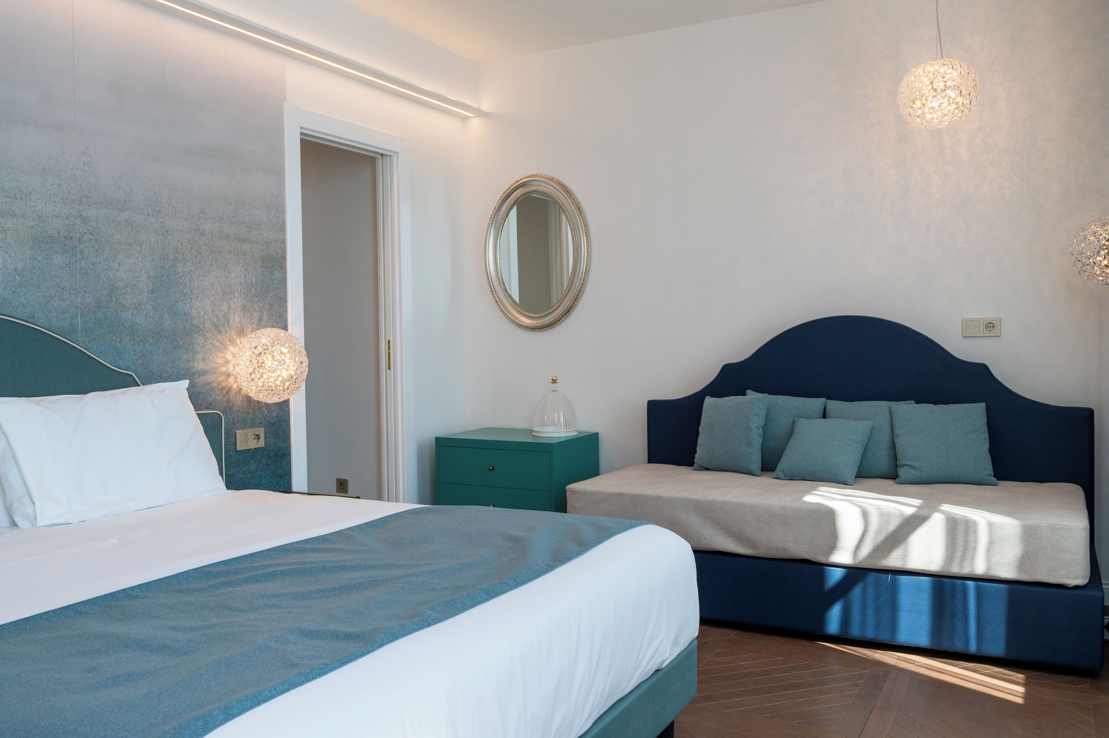 A bedroom with a bed, a sofa, a mirror, and two wall-mounted lights.