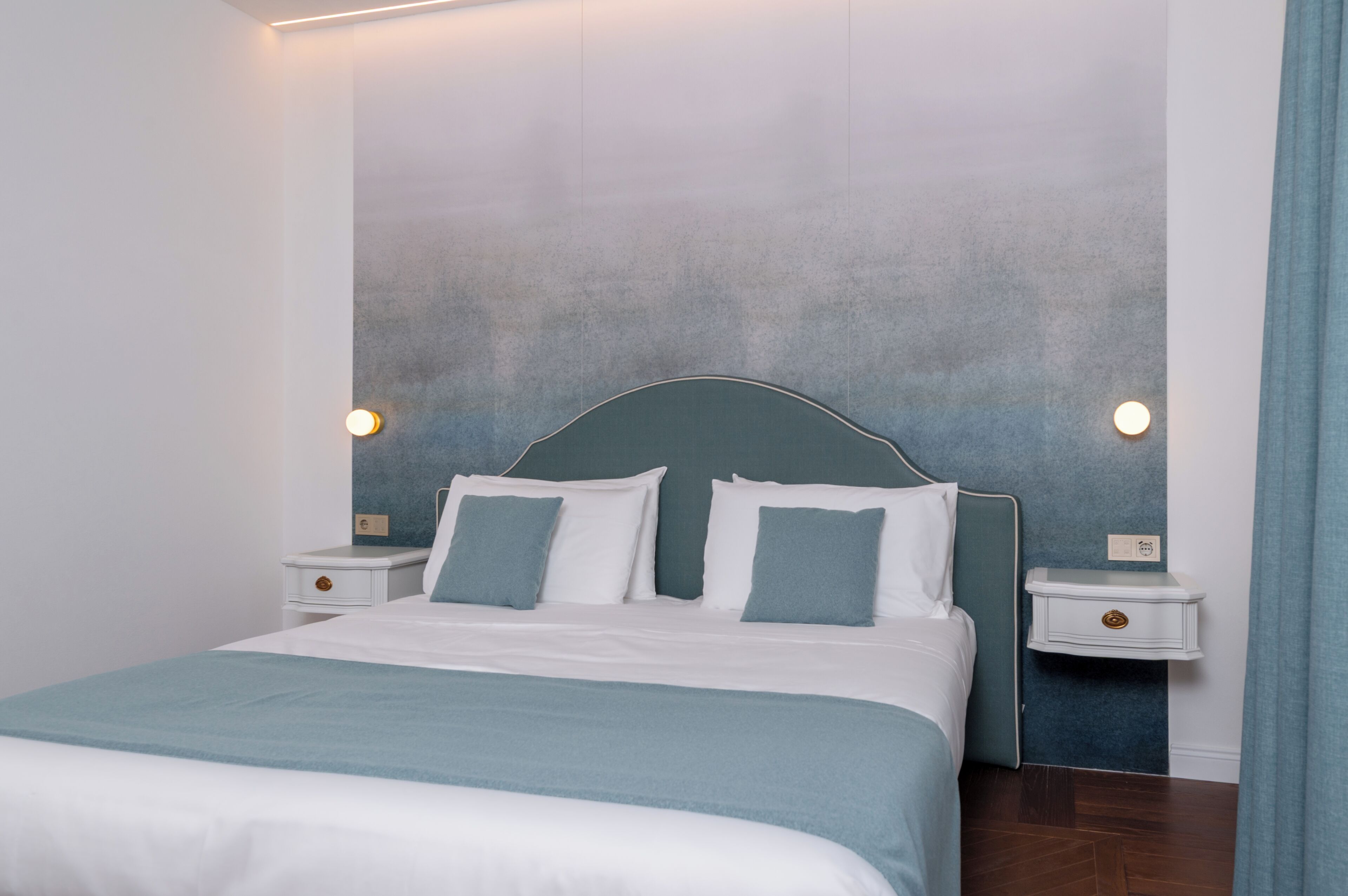 A bedroom with a bed, two bedside tables, and a wall-mounted light fixture.