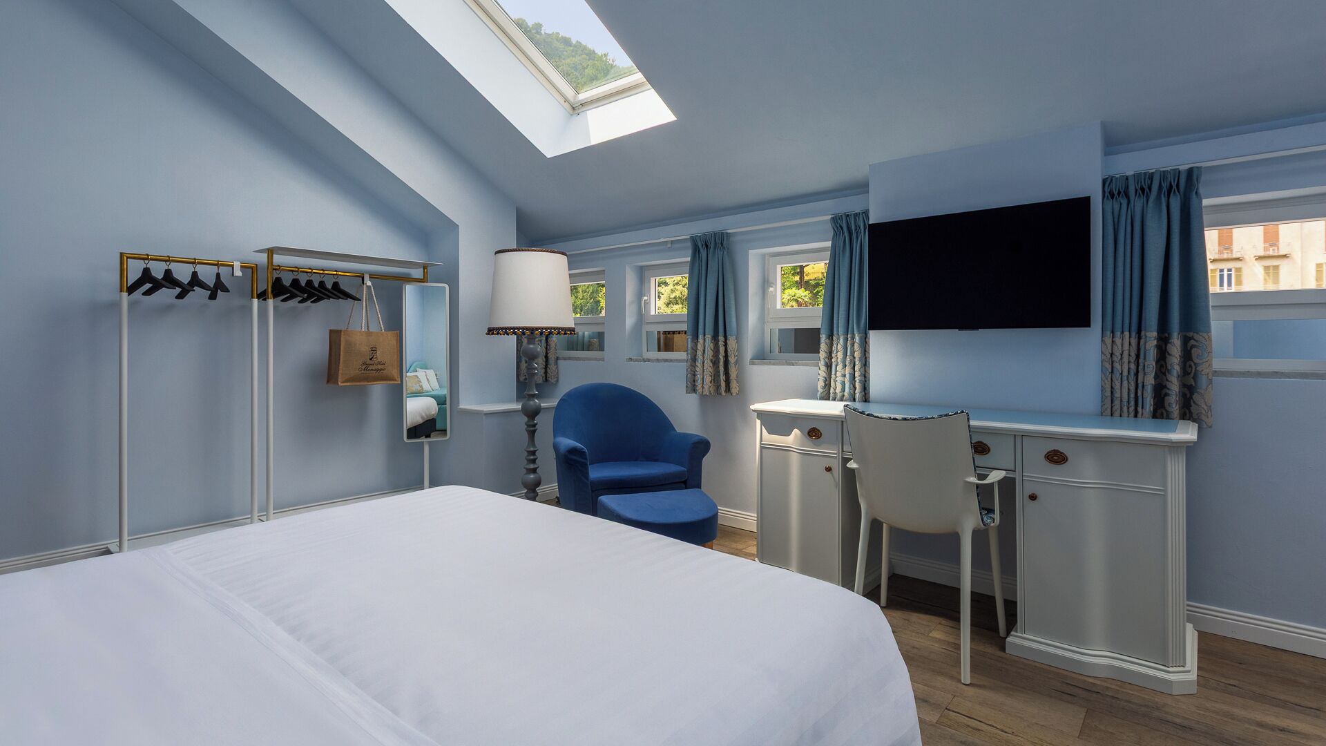 Una habitación de hotel con cama, escritorio, silla, espejo y armario.