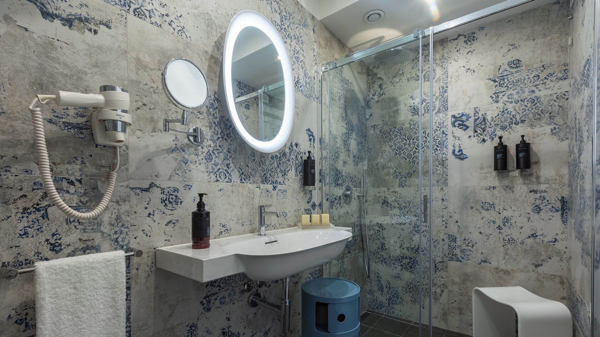 A bathroom with a modern design, featuring a large mirror, a sink with a towel, and a glass shower enclosure.