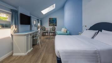 Una camera d'albergo con un letto, una scrivania, una sedia, un tavolino e un quadro appeso al muro.