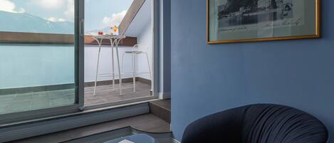 A balcony with a table and chairs, a framed picture on the wall, and a view of the sea.