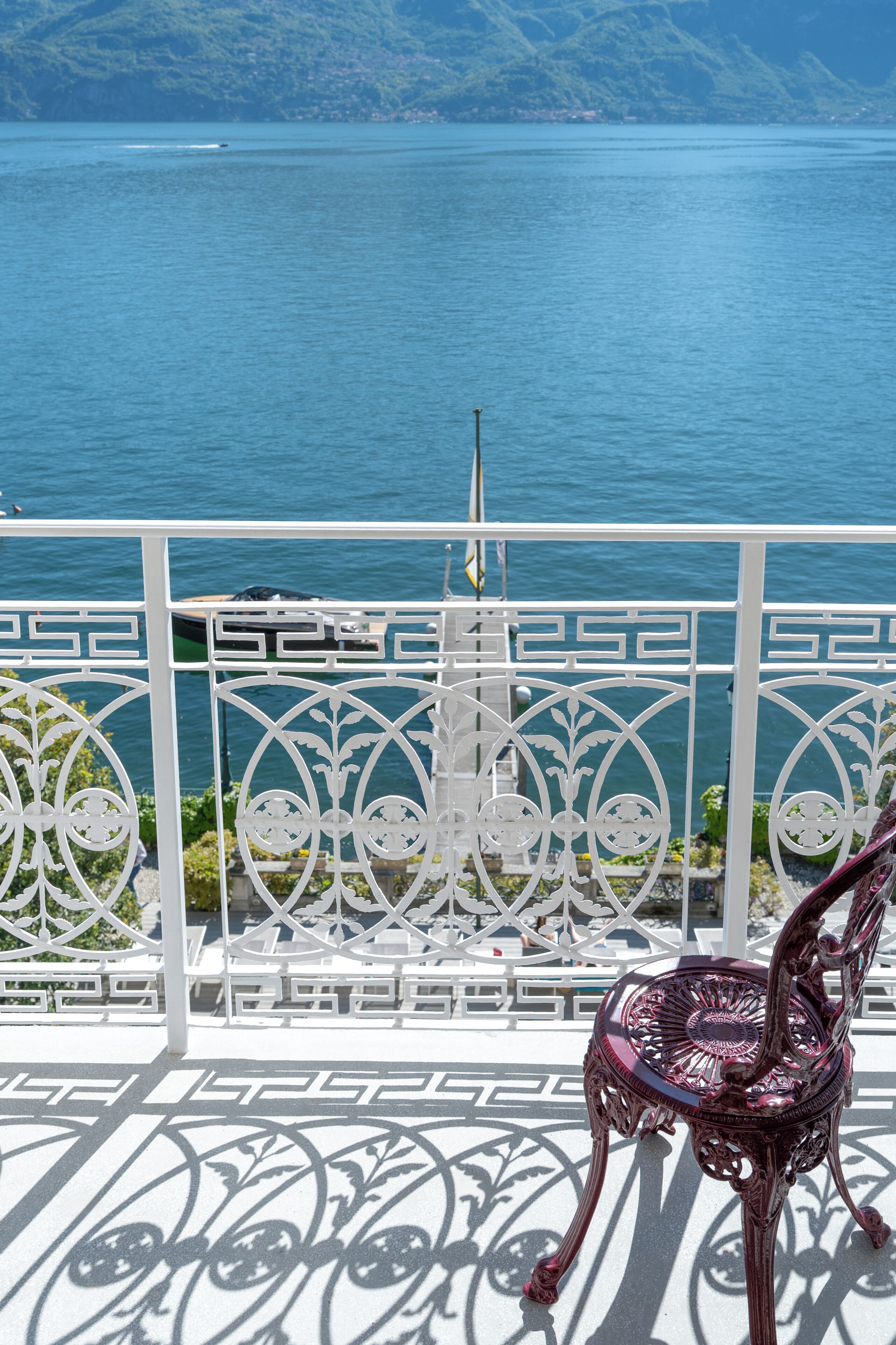 A balcony with a view of a body of water and mountains, a white metal railing, and a decorative chair.