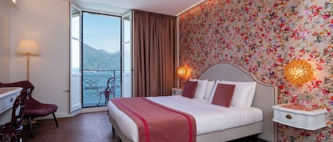 Habitación de hotel con cama, escritorio, silla, mesita de noche y vistas al exterior.
