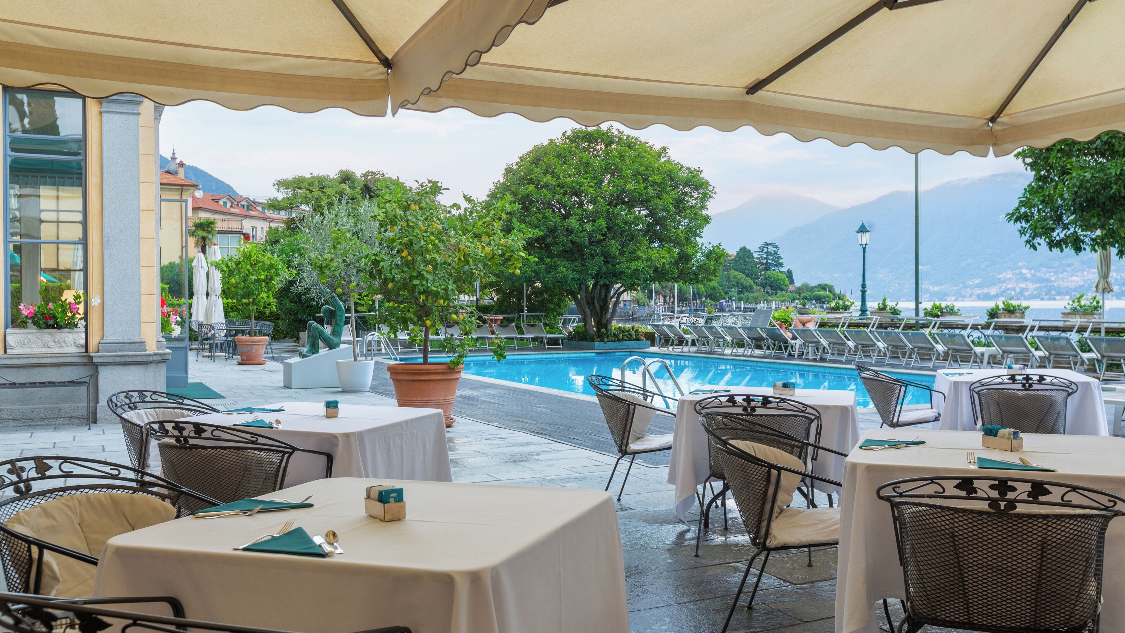 Un área de comedor al aire libre con mesas y sillas, una piscina y vistas a las montañas.