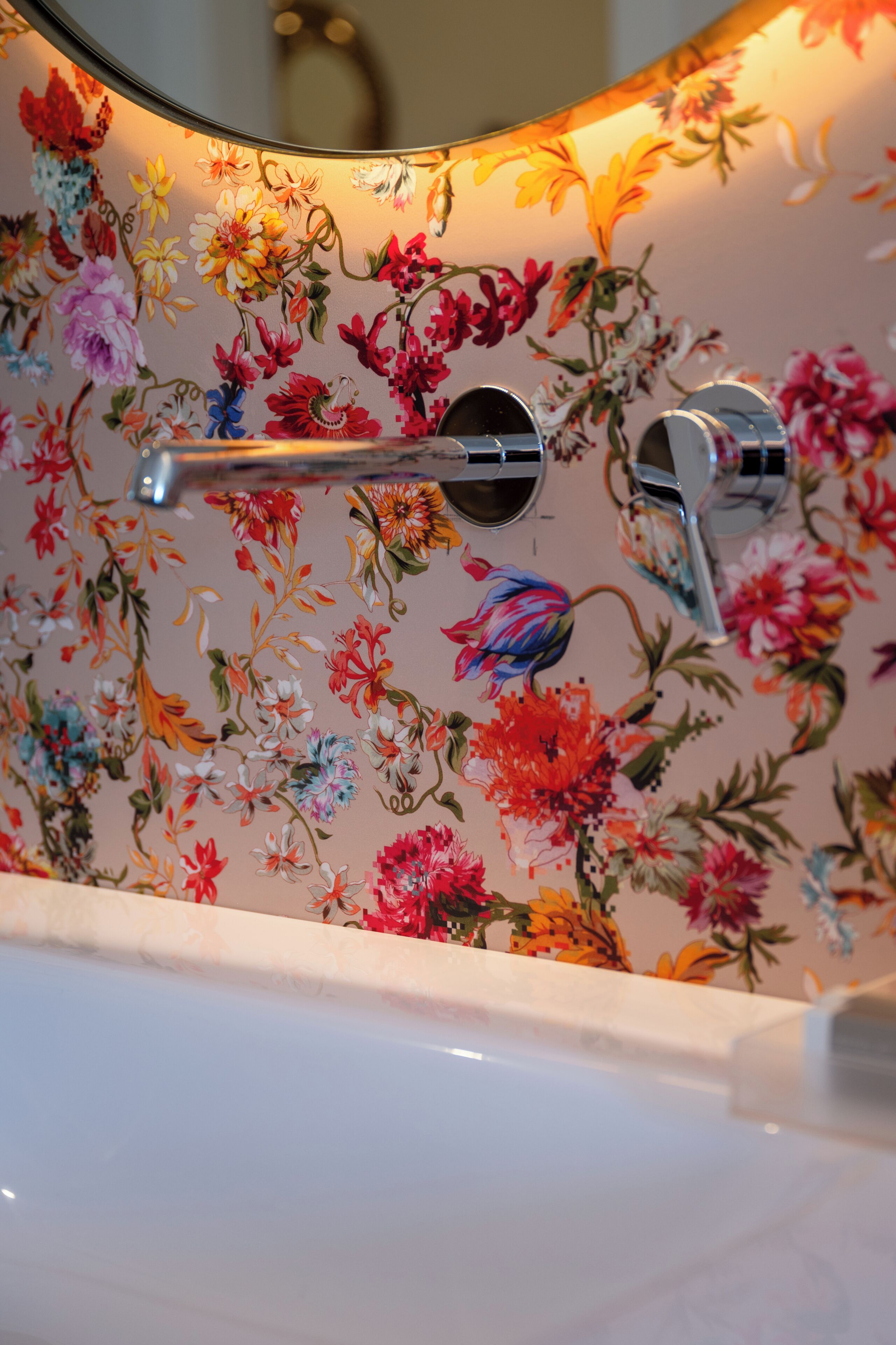 Ein Badezimmer mit floraler Tapete, einem Spiegel und einer Badewanne.