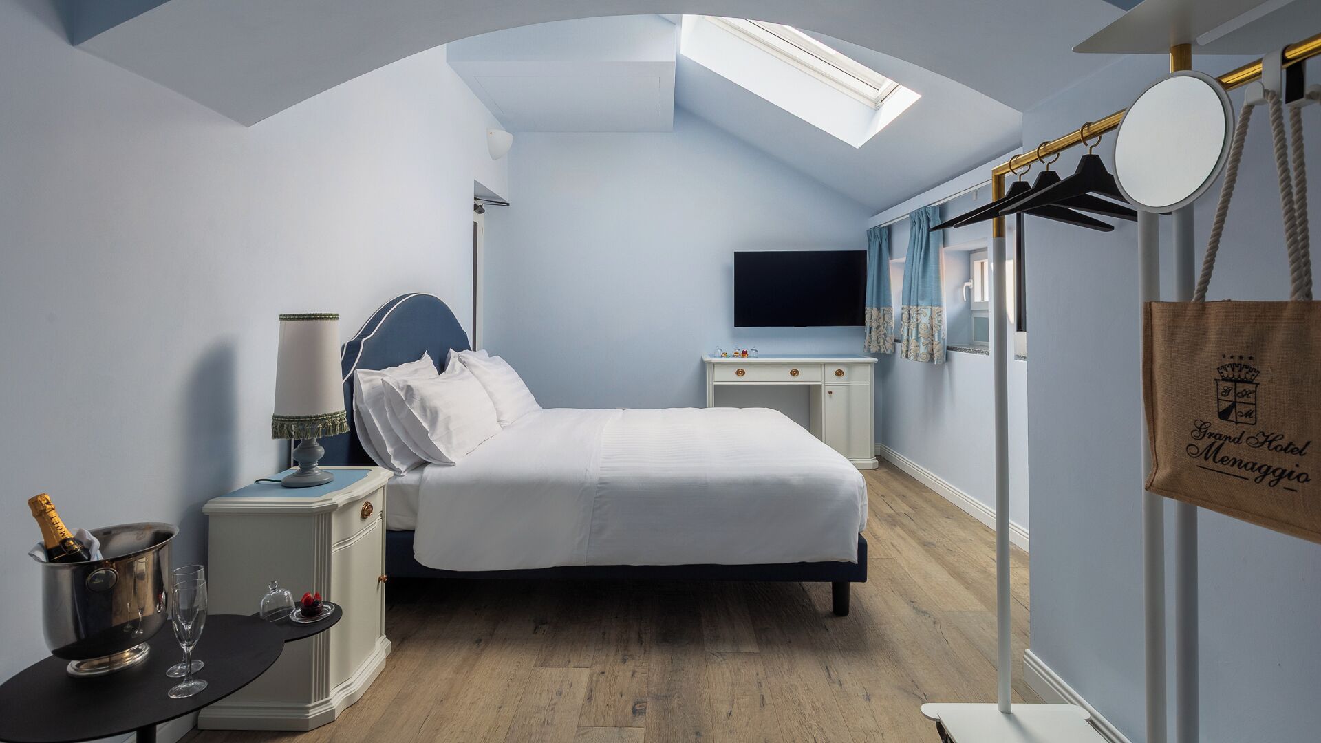A hotel room with a bed, bedside table, lamp, and a bottle of champagne.