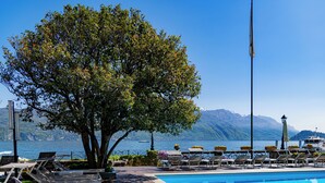 Un área junto a la piscina con sillas de descanso, un árbol y vista al agua.