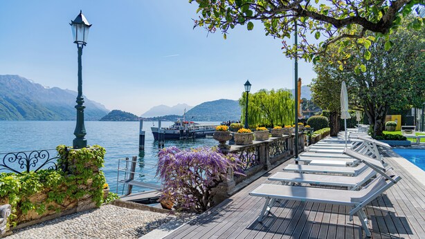 Una terraza de madera con bancos, una farola y macetas con flores a lo largo de un paseo marítimo junto al lago.
