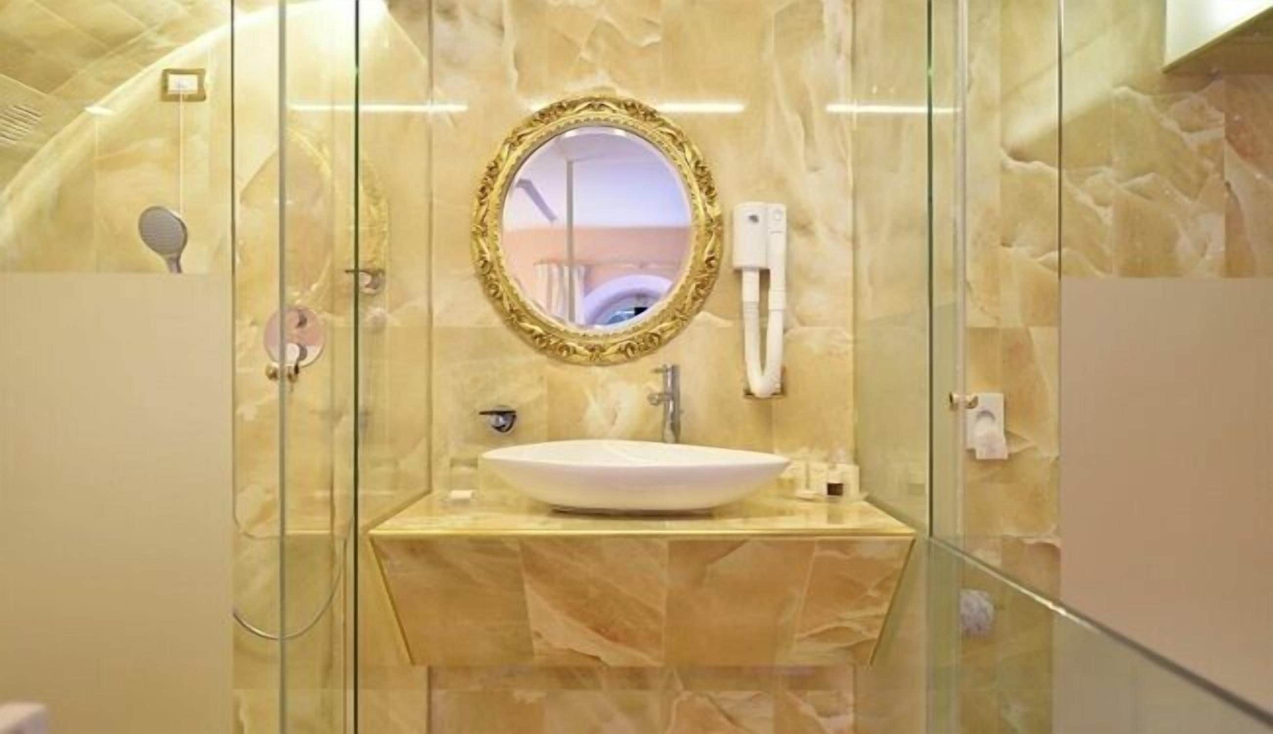 A modern bathroom with a marble vanity, a round mirror with an ornate frame, and a glass-enclosed shower area.