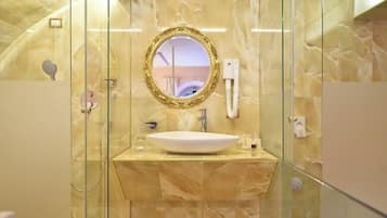 A modern bathroom with a marble vanity, a round mirror with an ornate frame, and a glass-enclosed shower area.