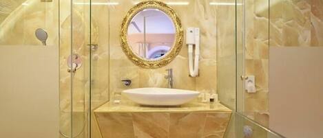 A modern bathroom with a marble vanity, a round mirror with an ornate frame, and a glass-enclosed shower area.