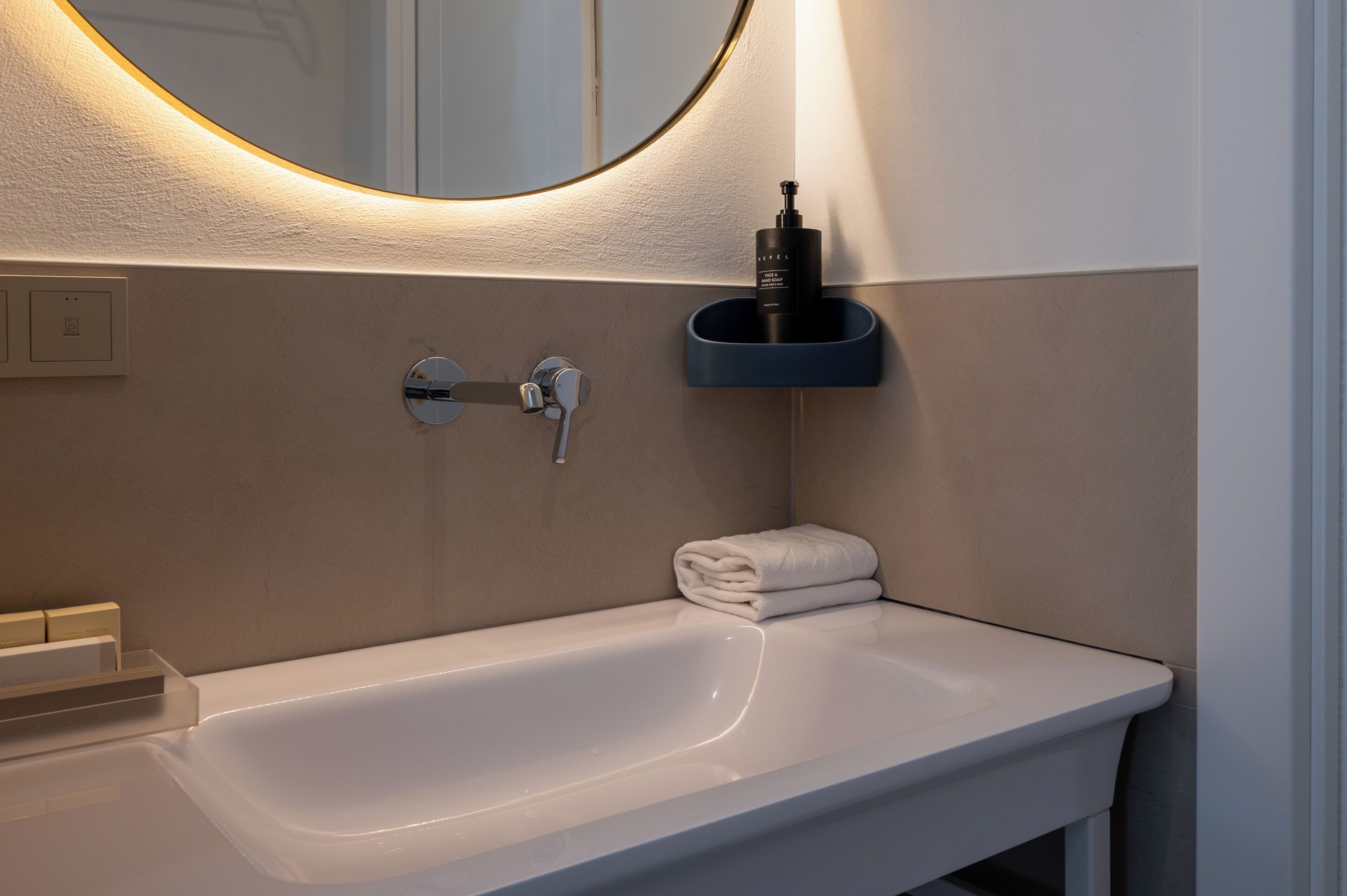 A bathroom with a white sink, a mirror, a towel, and a soap dispenser.