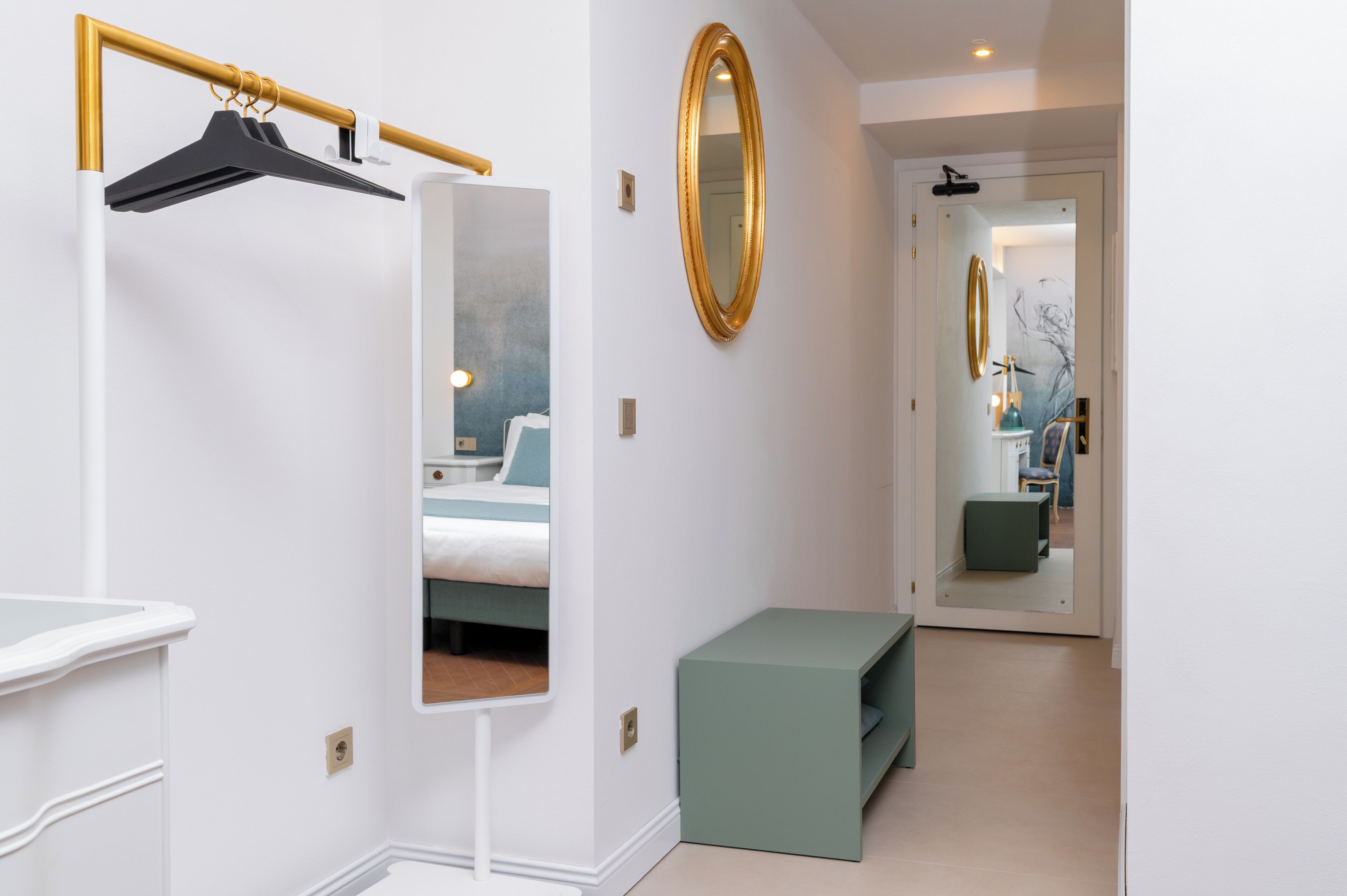Une chambre à coucher avec un lit, une table de chevet, un miroir et un banc vert.