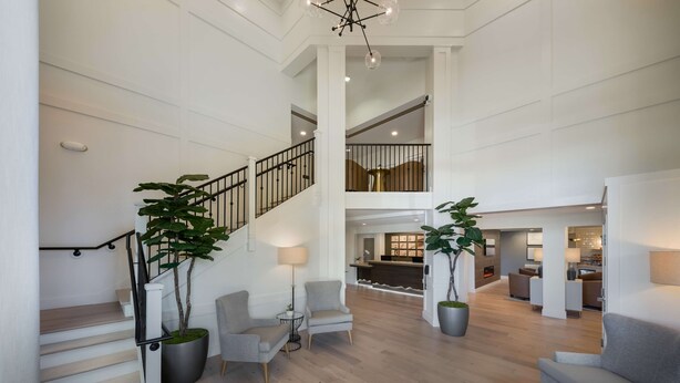 A spacious living area with a staircase, two potted plants, and a seating area with a lamp.