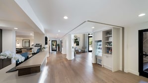 A spacious, modern interior with a long wooden floor, a reception desk, and a kitchen area visible through an open doorway.