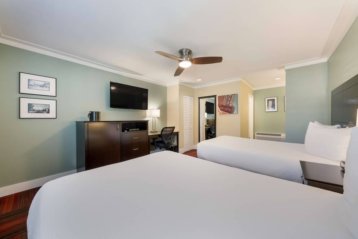 A hotel room with two beds, a desk with a chair, a television, and a ceiling fan.