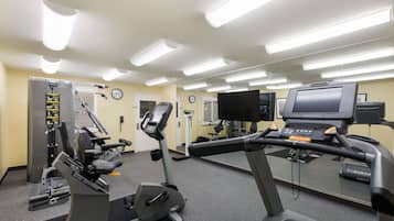 Et fitnessrum med løbebånd, styrkemaskiner og et spejl.