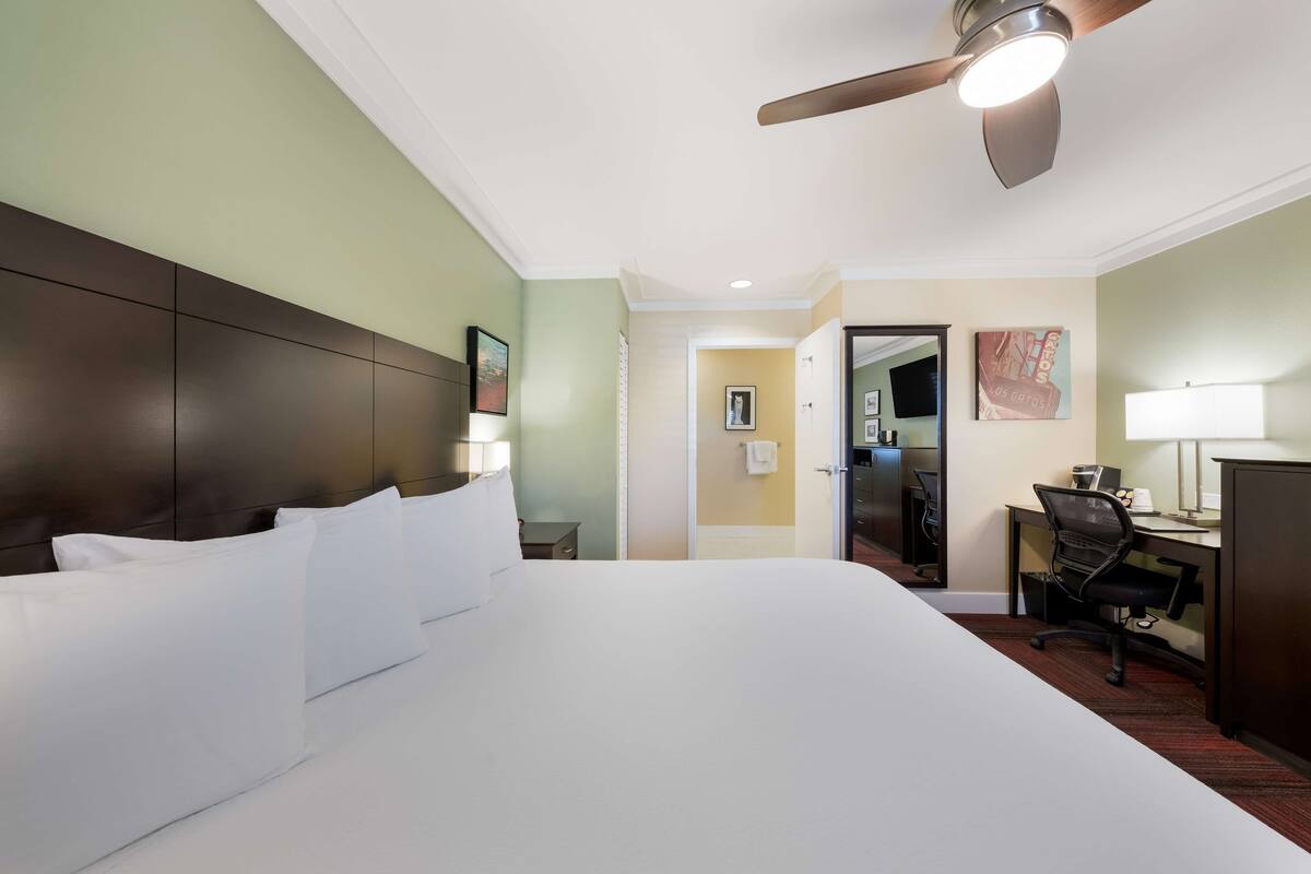 A hotel room with a large bed, a desk, a chair, and a ceiling fan.
