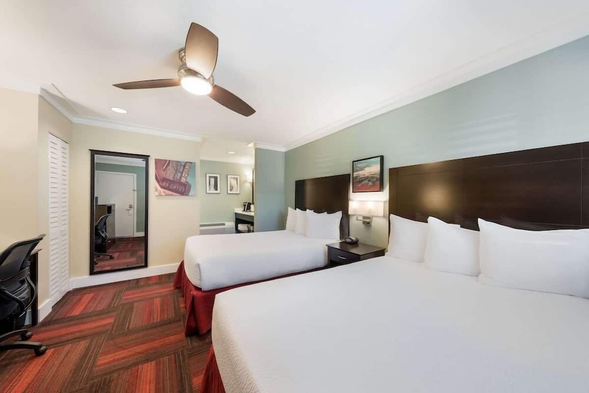 A hotel room with two beds, a ceiling fan, a desk, and a chair.
