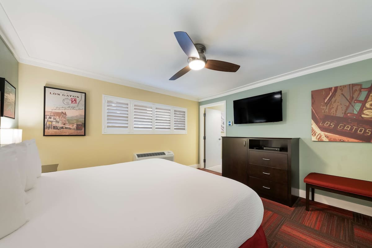 A hotel room with a large bed, a ceiling fan, a TV, a wardrobe, and a bench.