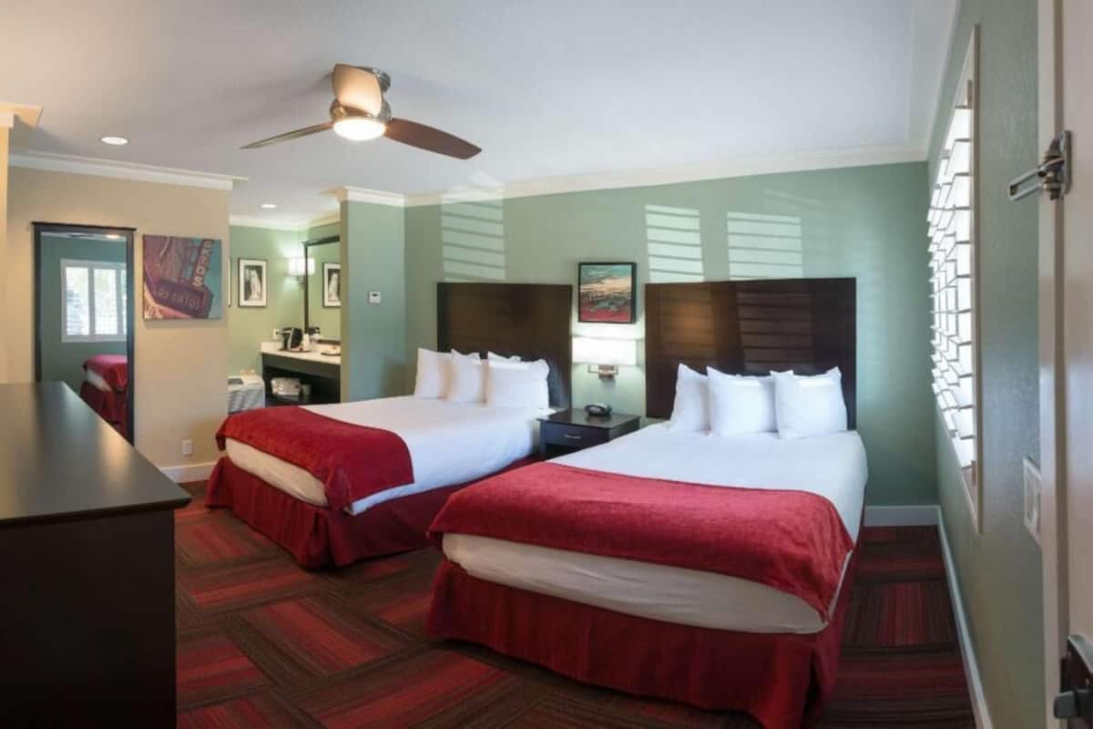 A hotel room with two beds, a desk, a ceiling fan, and a view of the city.
