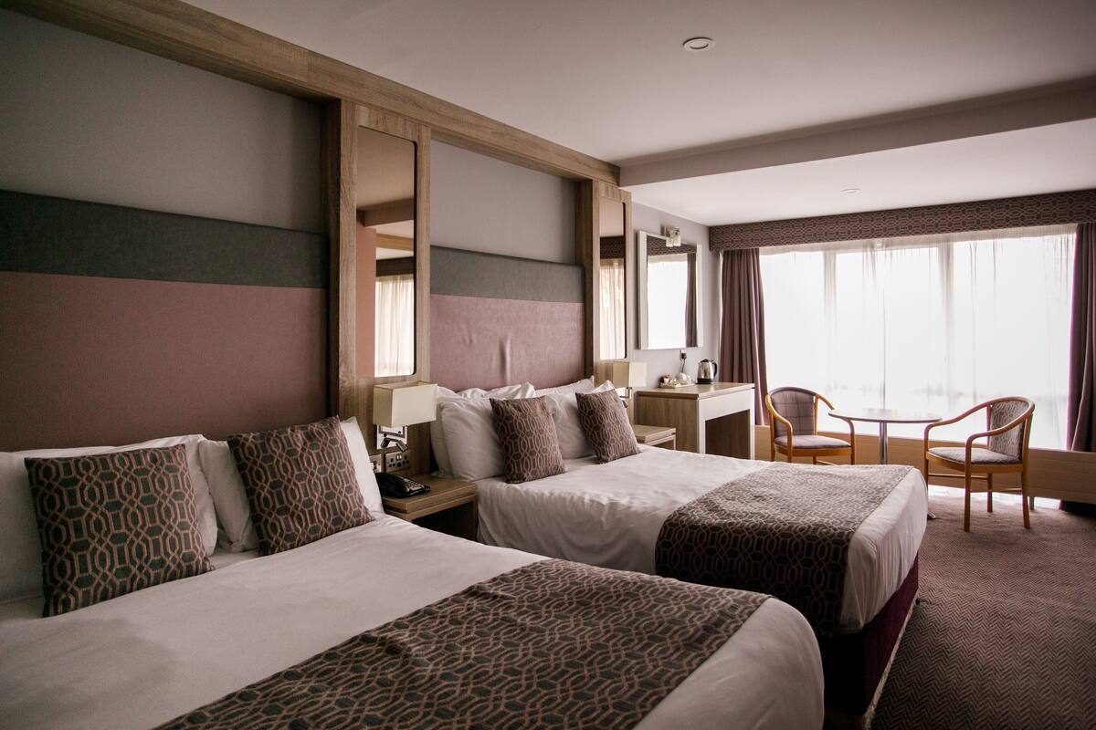 Ein Hotelzimmer mit zwei Betten, einem Schreibtisch, einem Stuhl und einem großen Fenster.