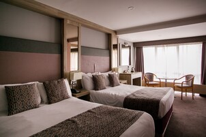 Habitación de hotel con dos camas, un escritorio, una silla y un ventanal grande.