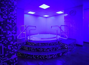 A hot tub with steps and railings, surrounded by walls with a mosaic tile pattern.