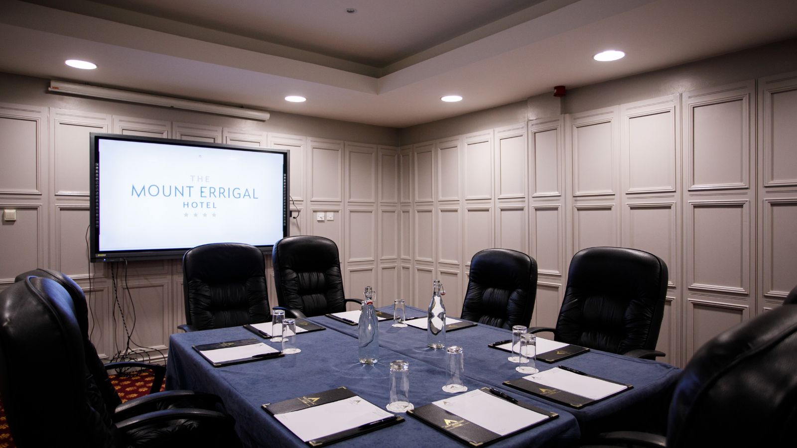 A conference room with a long table, black leather chairs, a projector screen, and a whiteboard.