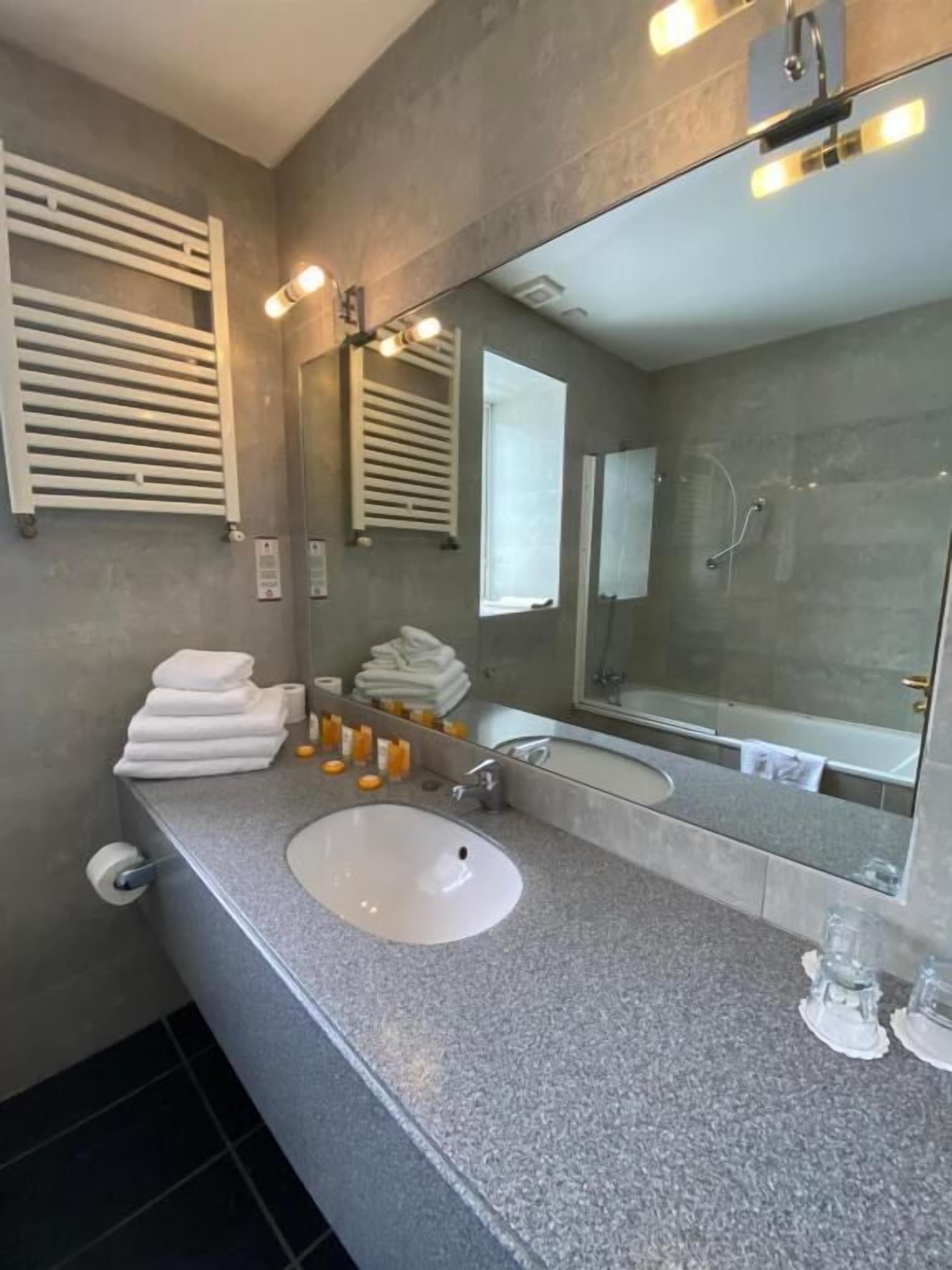 Un baño moderno con un espejo grande, un lavamanos blanco y una ducha.
