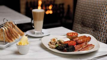 A breakfast setting with toast, a cup of coffee, beans, sausages, mushrooms, and a plate of eggs.