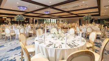 Un salón de banquetes con mesas redondas dispuestas para un evento formal, con manteles blancos, sillas doradas y centros de mesa florales.