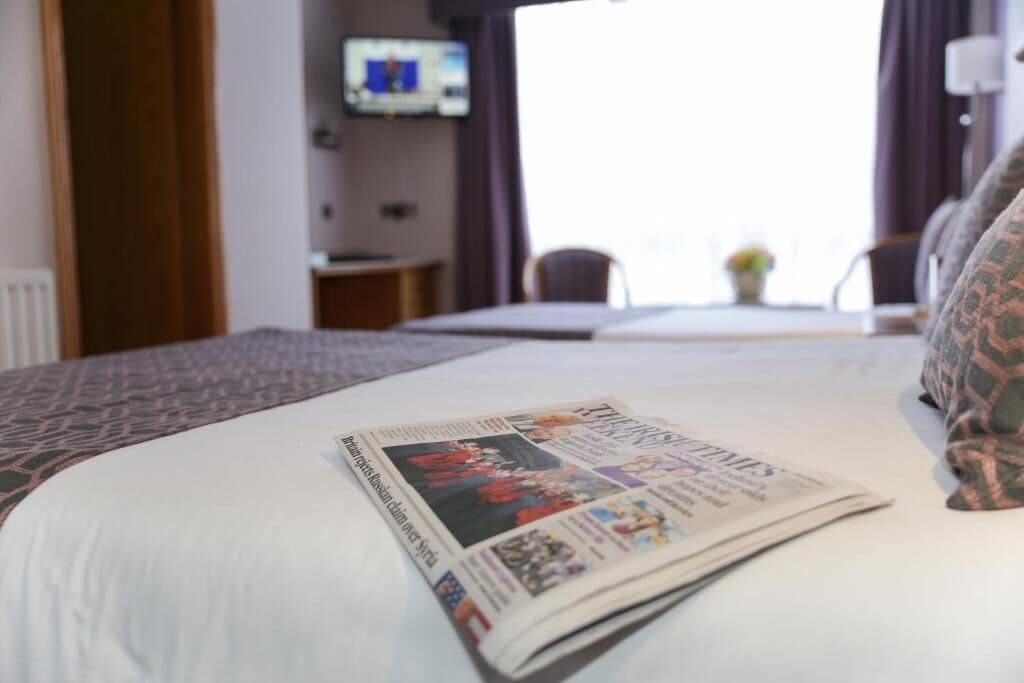 Quarto de hotel com cama bem arrumada, televisão na parede e janela com cortinas.
