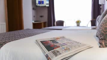 A hotel room with a neatly made bed, a television on the wall, and a window with curtains.