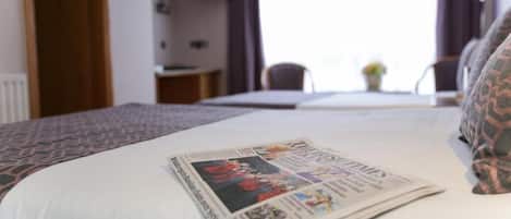 A hotel room with a neatly made bed, a television on the wall, and a window with curtains.