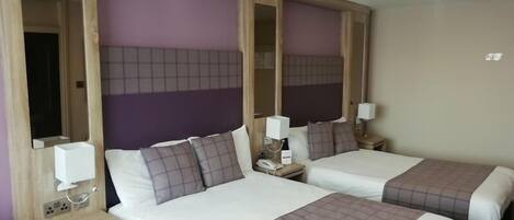 A hotel room with two beds, each with a nightstand, a mirror, and a lamp.