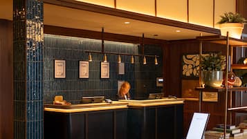 A hotel reception area with a check-in counter, a reception desk, and a wall-mounted information board.