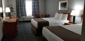 Two single beds with brown headboards and white bedding, a desk with a telephone and lamp, and a chair.