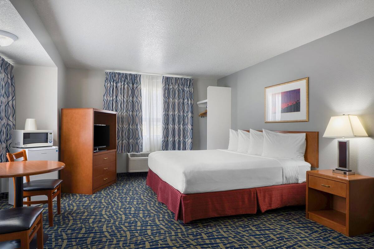 A hotel room with a bed, a desk, a microwave, a TV, and a window with curtains.
