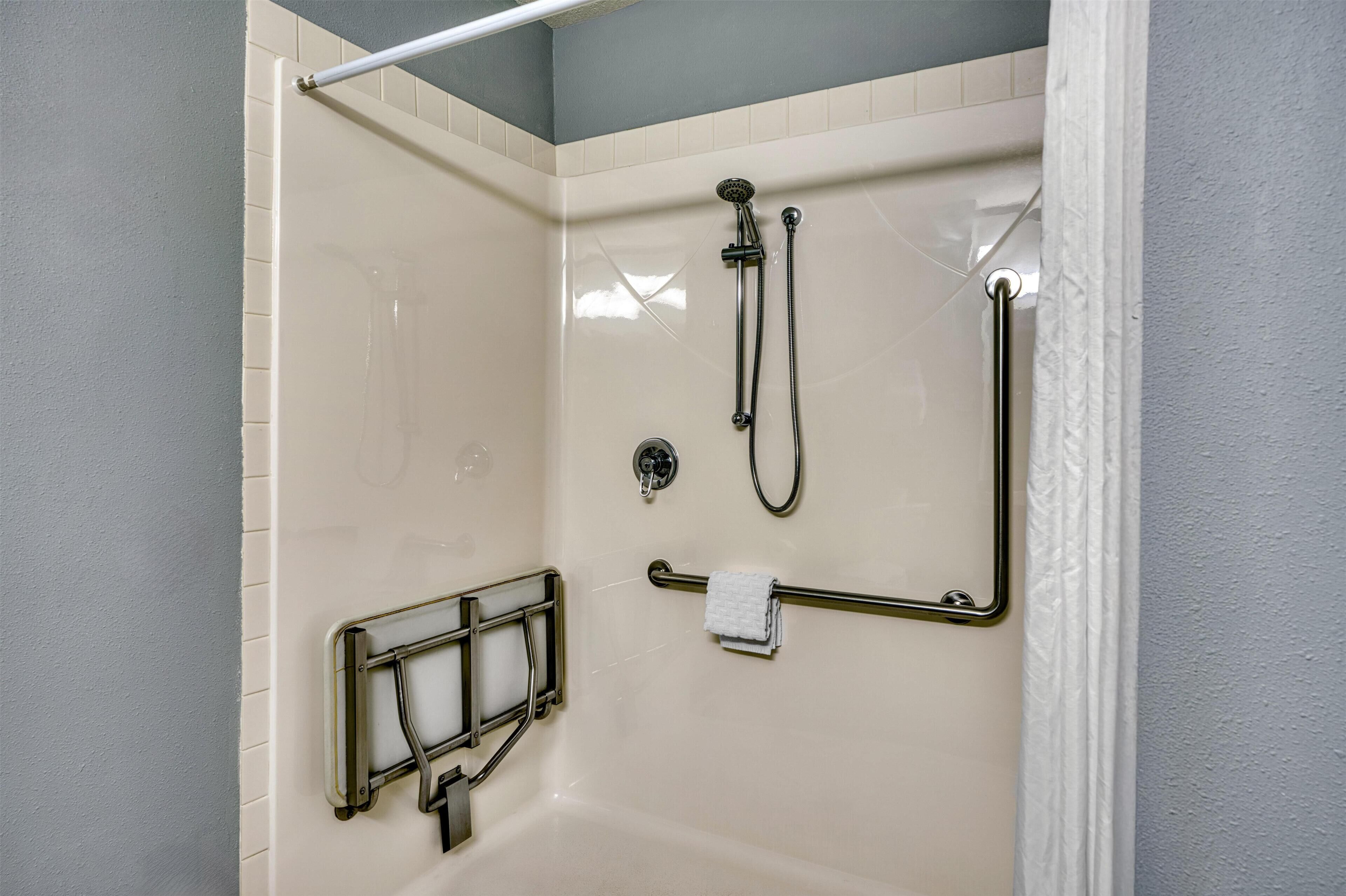 A shower area with a grab bar, a towel rack, and a handheld showerhead.