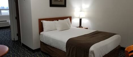 A hotel room with a bed, a nightstand, a lamp, a chair, and a window.