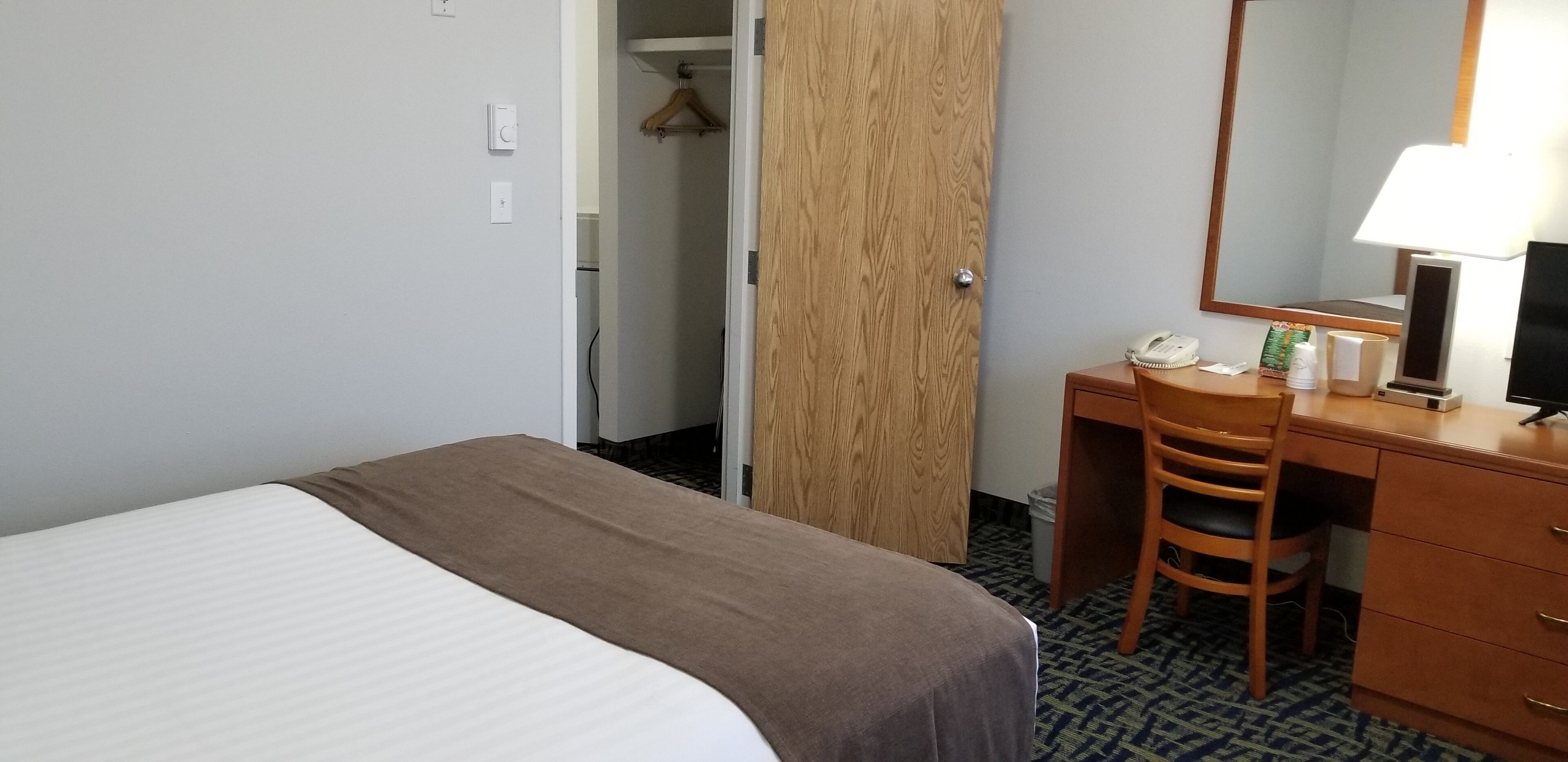 A hotel room with a bed, a desk, a chair, a mirror, a telephone, and a wardrobe.
