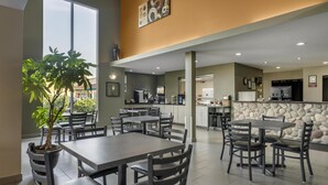 A modern dining area with multiple tables and chairs, a potted plant, and a stone accent wall. - SureStay Plus Hotel by Best Western Lethbridge (Lethbridge)