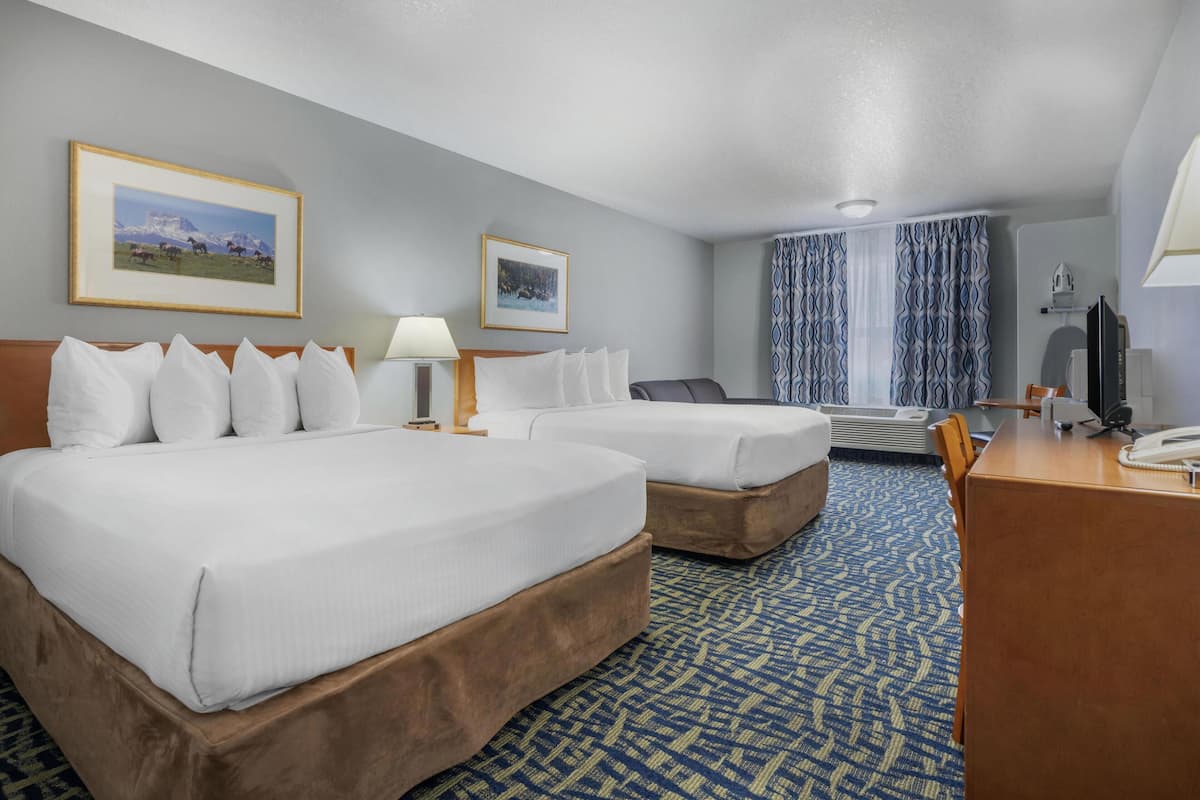 A hotel room with two beds, a desk, a chair, a TV, and a window with curtains.