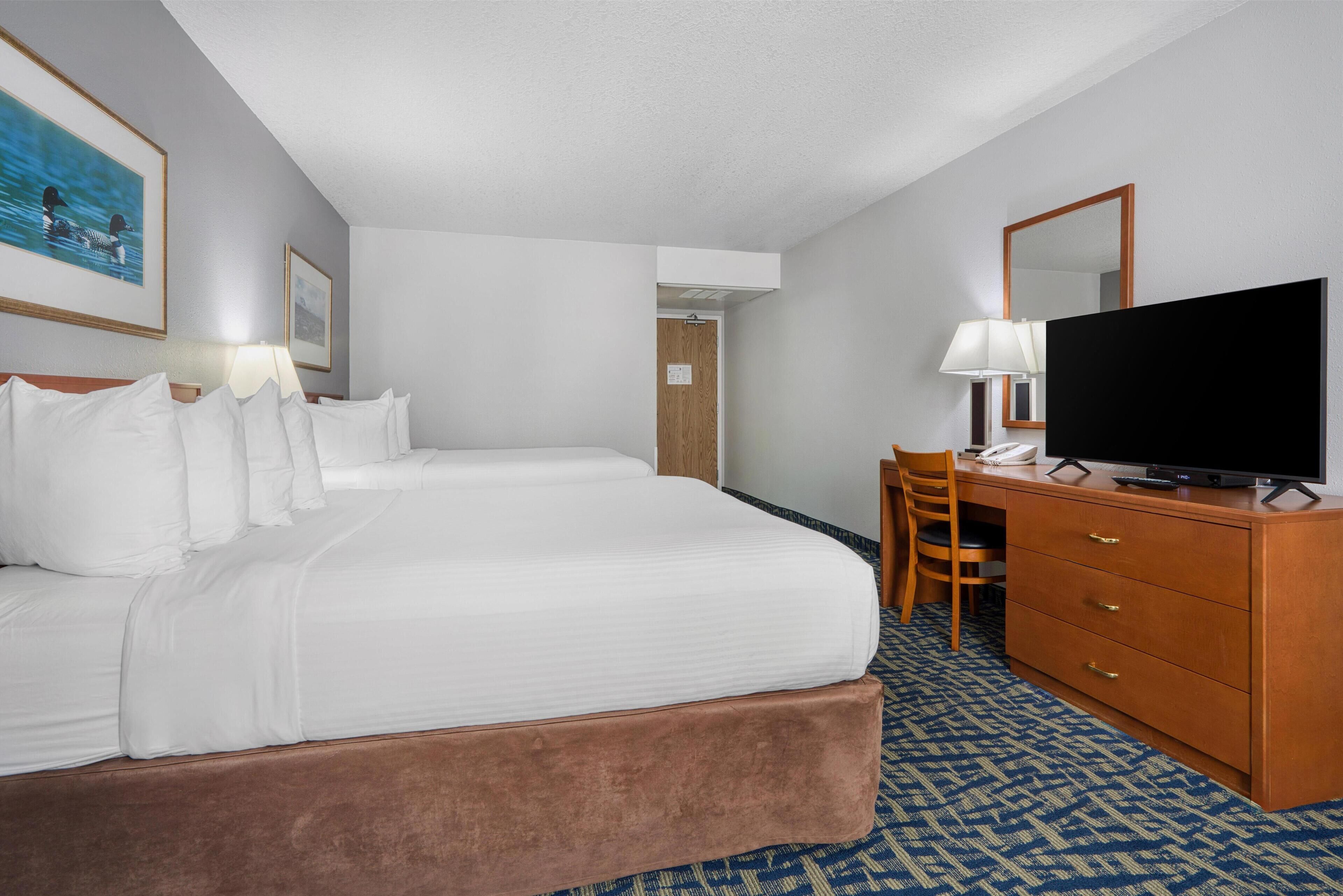 A hotel room with two beds, a desk, a television, and a patterned carpet.