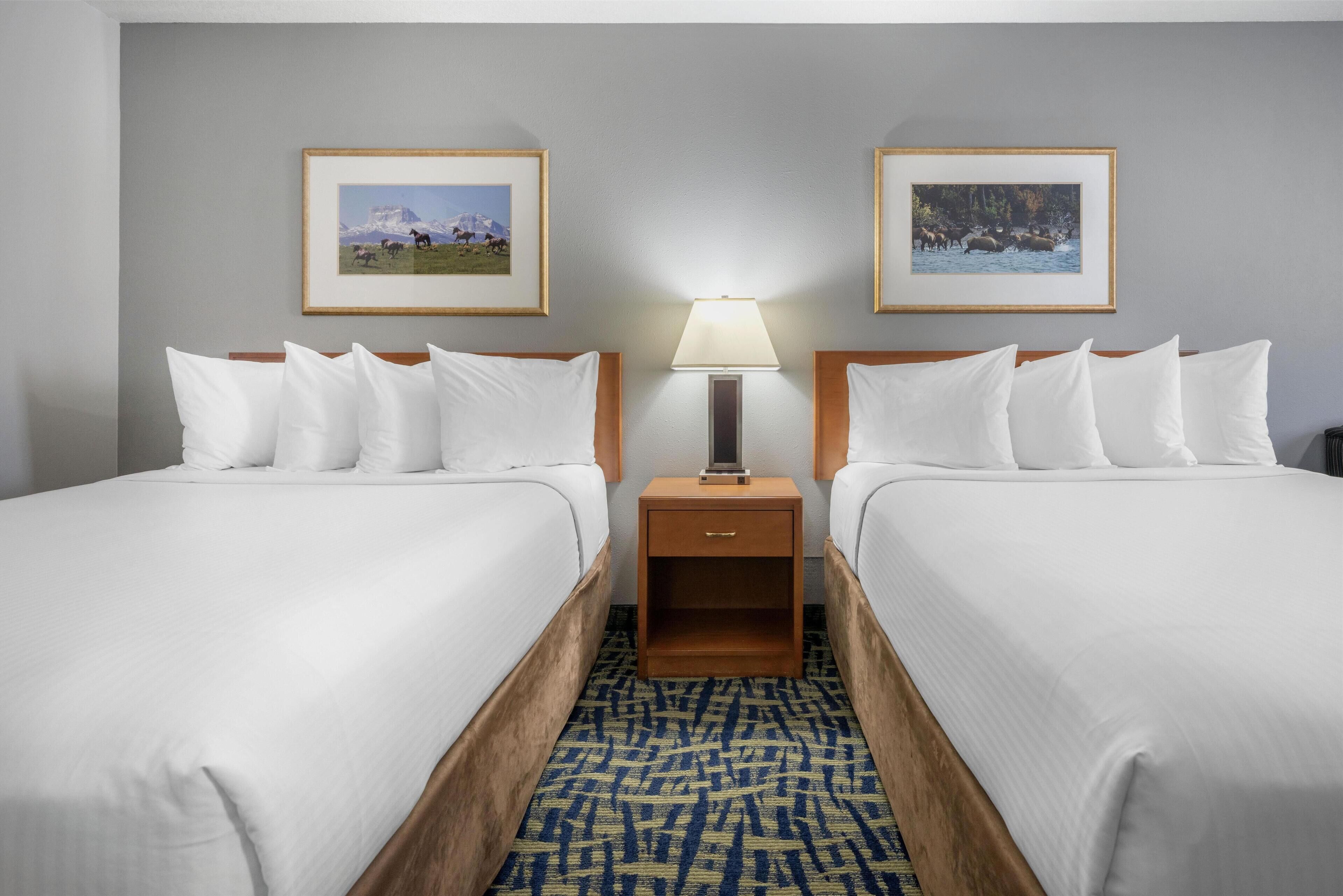 Una habitación de hotel con dos camas, una mesita de noche con lámpara y cuadros en la pared.