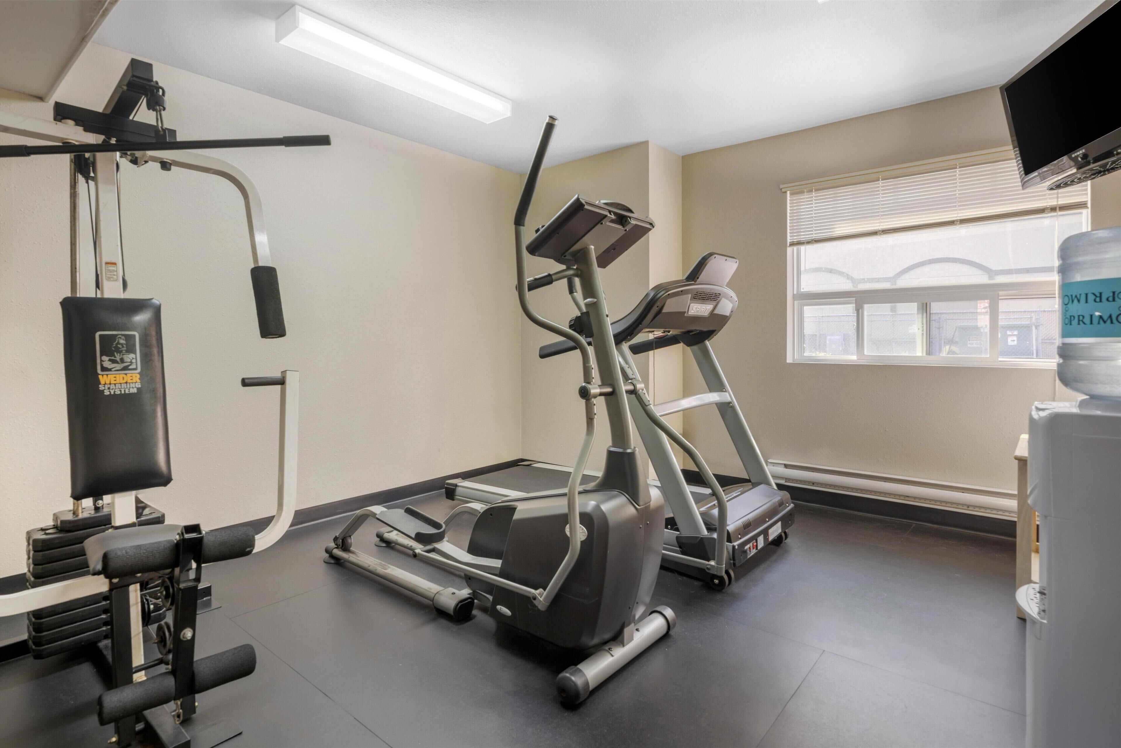 A gym with a treadmill, elliptical, and weight machine.